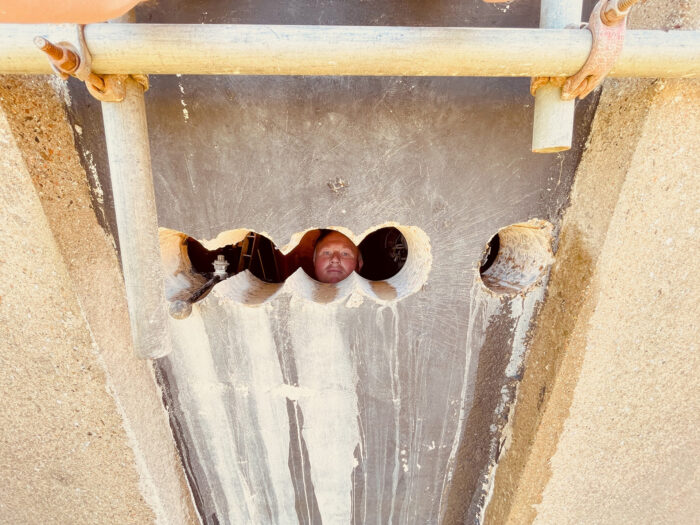 A workman peering through the hole in the concrete that he has just cut